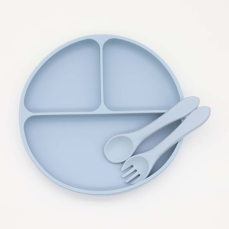 Assiette à dîner ronde en silicone pour bébé avec ventouse et compartiments, accompagnée d'une cuillère et d'une fourchette.
